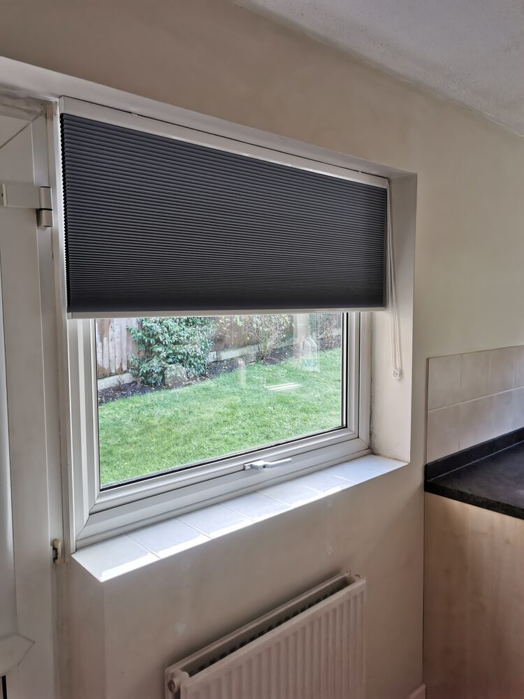 Free-hanging pleated blind in a kitchen window looking out onto a garden