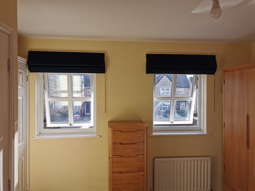 Pair of navy velour blackout Roman blinds in a bedroom