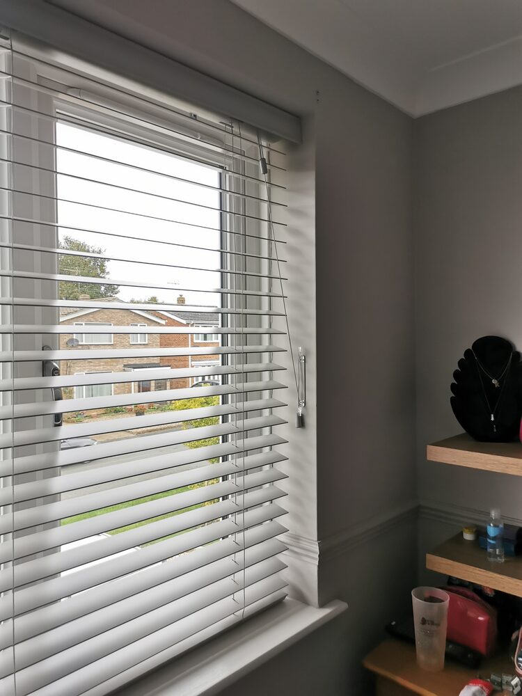 Pale grey wooden Venetian blind in a bedroom window